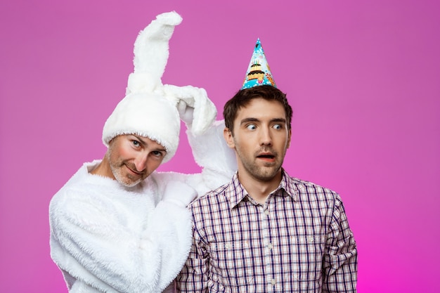 Free photo drunk man and rabbit at birthday party over purple wall.