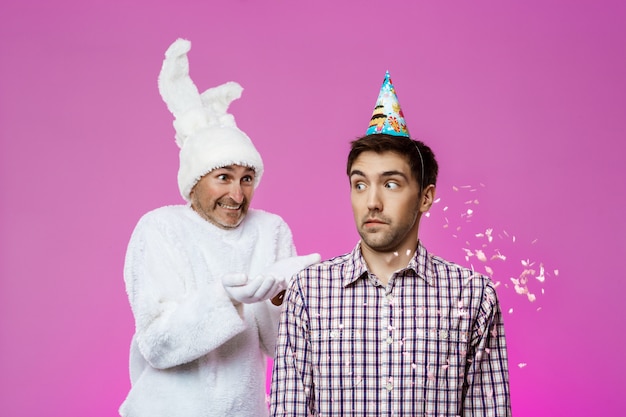 Free photo drunk man and rabbit at birthday party over purple wall.