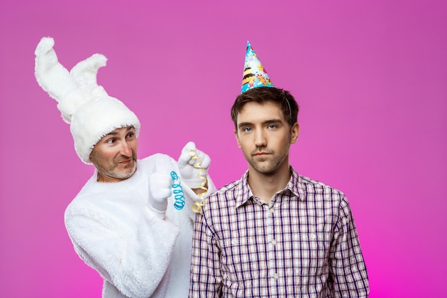 Drunk man and rabbit at birthday party over purple wall.