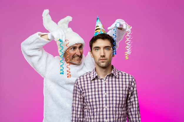 Drunk man and rabbit at birthday party over purple wall.