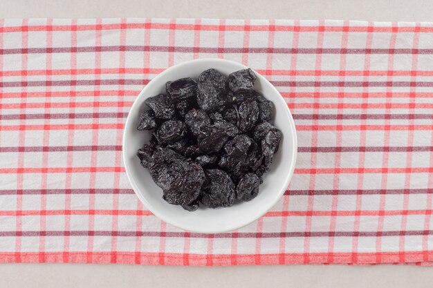 Dry black plums in a ceramic cup on concrete.