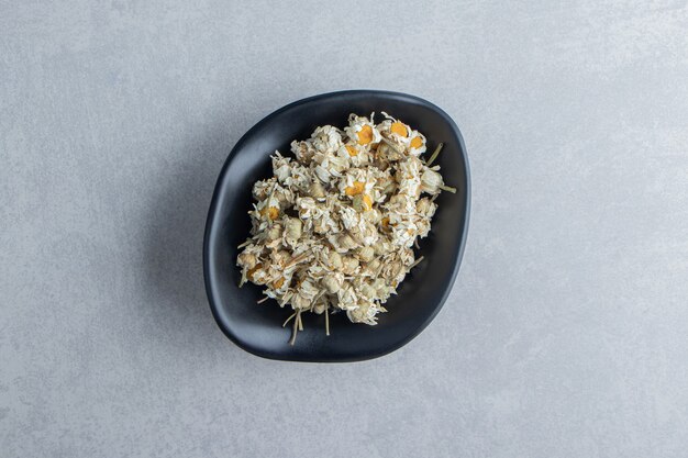 Dry chamomile flowers in black bowl.  