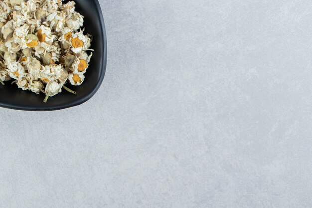 Dry chamomile flowers in black bowl.  