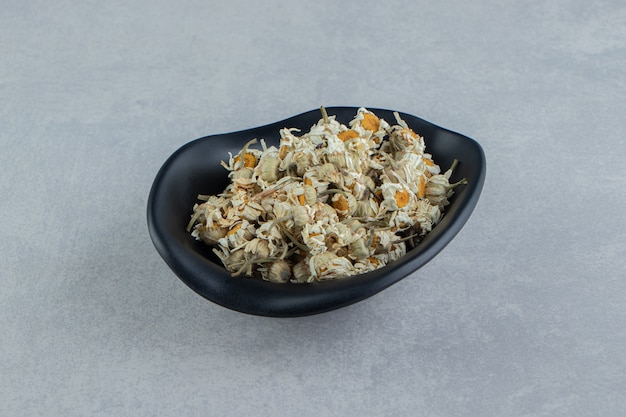 Dry chamomile flowers in black bowl