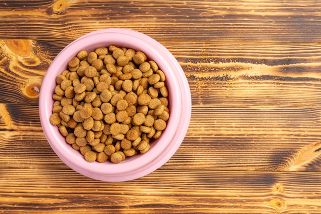 Dry dog food in bowl on dark wooden surface