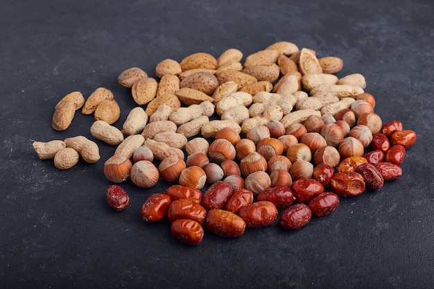 Dry fruits and beans on black surface, angle view. 