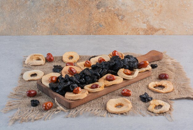 Dry fruits including apple slices, black sultana and jujube berries on concrete surface.