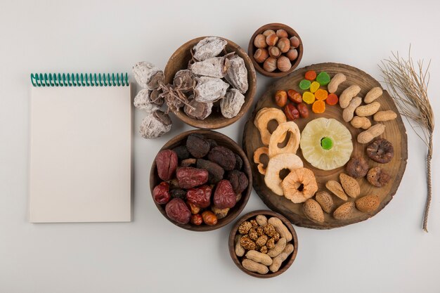 Dry fruits and snacks in multiple wooden platters and saucers with a notebook aside