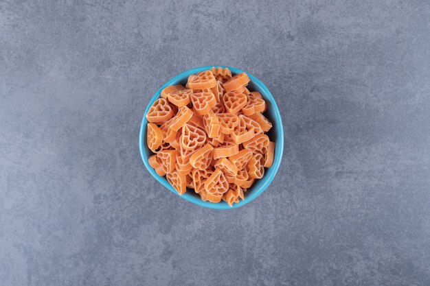 Dry heart-shaped pasta in blue bowl. 