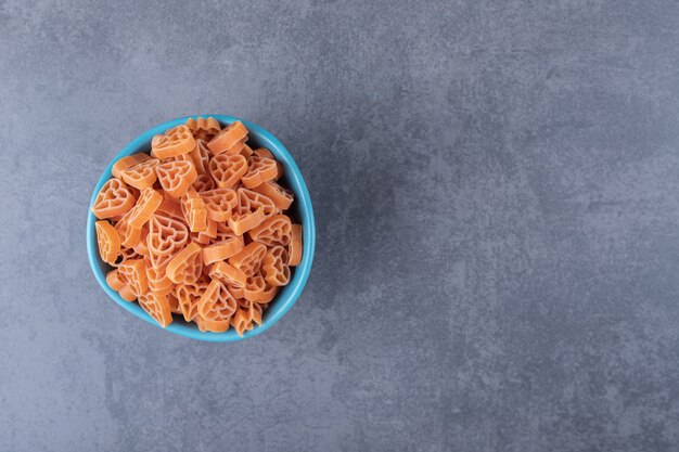Dry heart-shaped pasta in blue bowl.