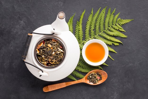 Dry herb leaves and fern leaves with herbal tea on black surface