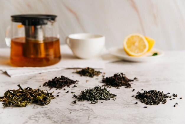 Dry herbal tea leaves with tea and lemon on marble textured backdrop