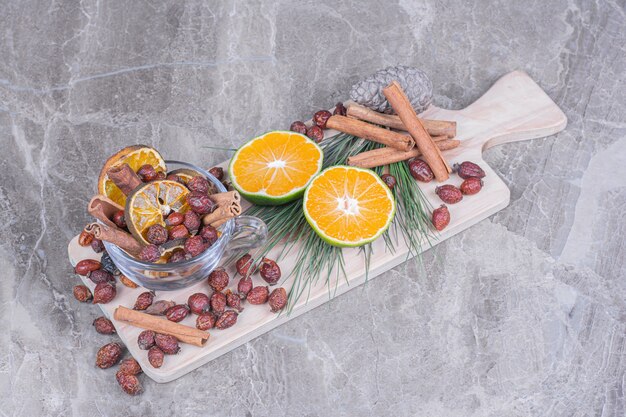 Dry hips and orange slices with fresh oranges on wooden board.