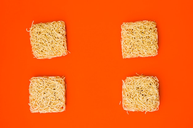 Dry instant noodles arranged on plain bright orange surface