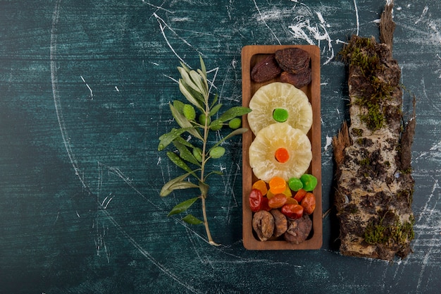 Dry and jelly fruits board with a piece of wood on a blue table