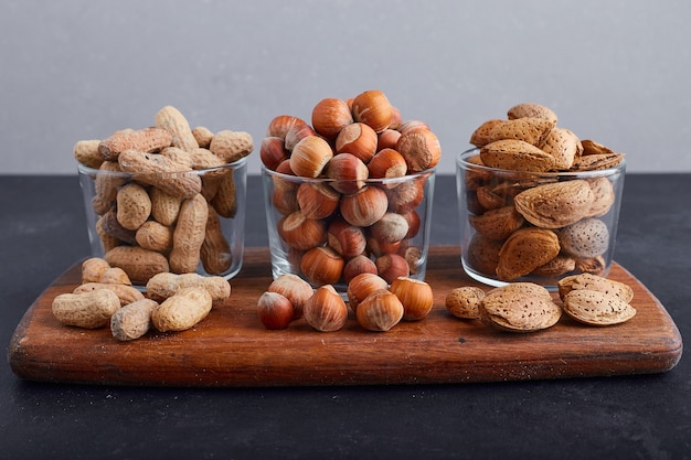 Dry nuts in glass cups on a wooden platter on blue background. 