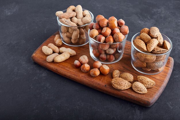 Dry nuts in glass cups on a wooden platter, top view. 