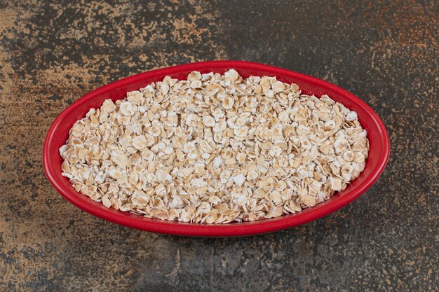 Dry oat flakes in red bowl. 