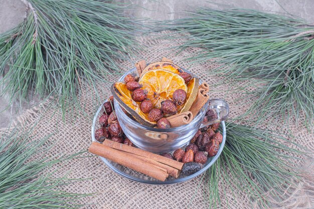 Dry orange slices with hips and cinnamons in a glass cup.