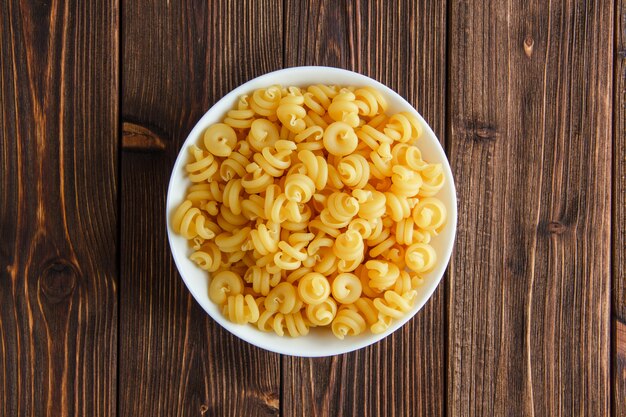 Dry pasta in a bowl on a wooden table. flat lay.