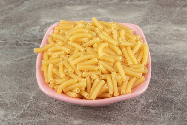 Dry pasta shaped like narrow tubes in pink bowl