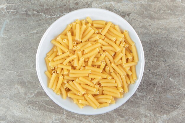 Dry pasta shaped like narrow tubes in white bowl