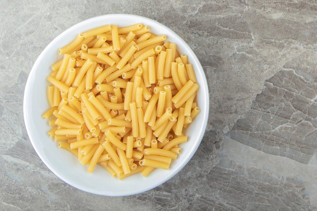 Dry pasta shaped like narrow tubes in white bowl.