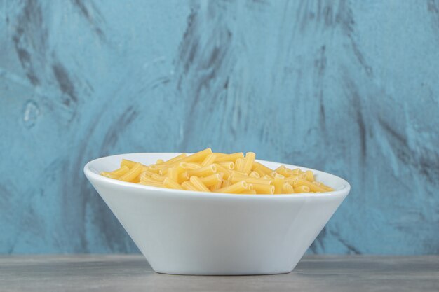 Dry pasta shaped like narrow tubes in white bowl.