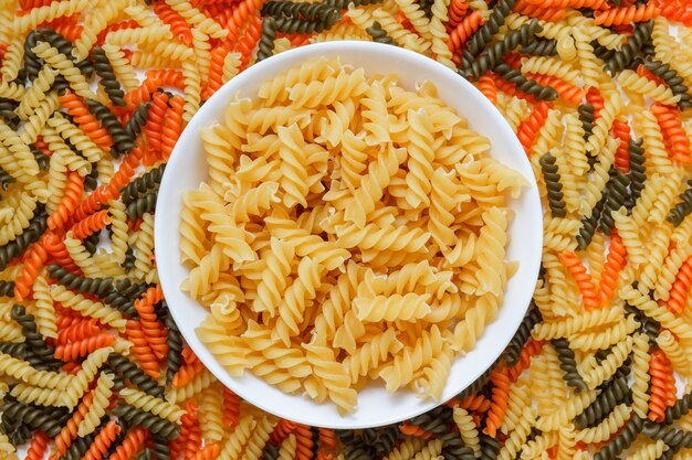 Dry pasta in a white plate on macaroni table, flat lay.