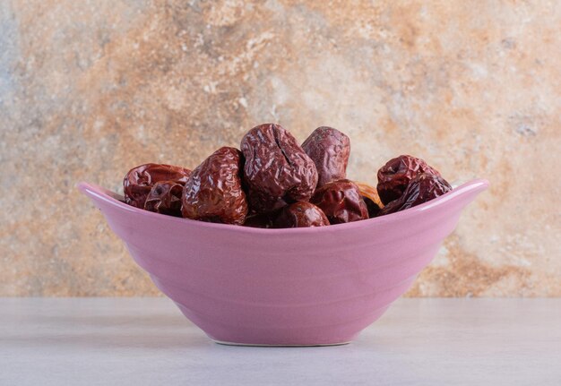 Dry red jujube berries in a purple bowl.