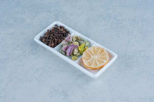 Высушите нарезанный лимон, чайные листья и цветок в миске на мраморе.