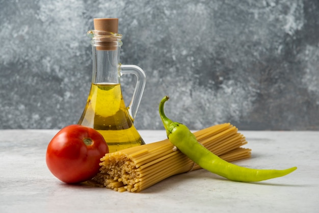 Foto gratuita spaghetti secchi, bottiglia di olio d'oliva e verdure sulla tavola bianca.