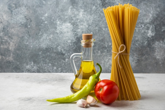 Dry spaghetti, bottle of olive oil and vegetables on white table. 