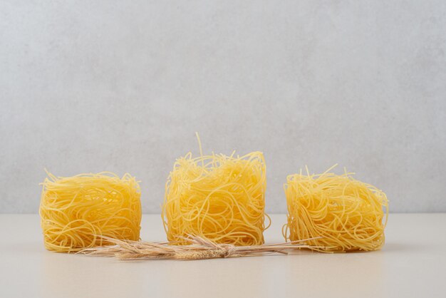 Сухие спагетти гнездятся на белой поверхности с пшеницей