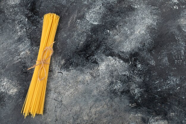 Dry spaghetti tied with rope on marble surface