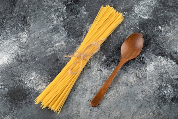 Dry spaghetti and wooden spoon on marble surface