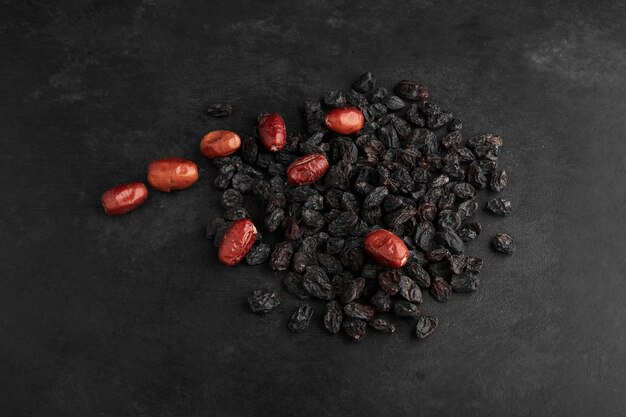 Dry sultanas and dates on black surface. 