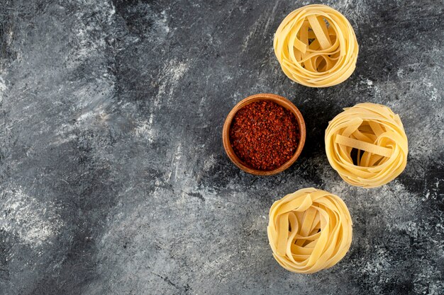 Dry tagliatelle nests and ground red pepper on marble surface