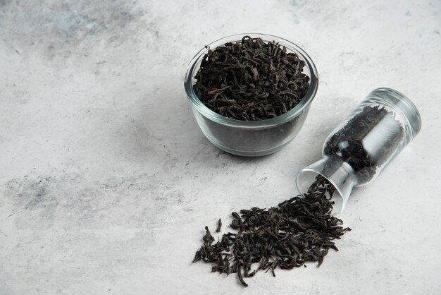 Dry tea leaves in a glass bowl on marble.