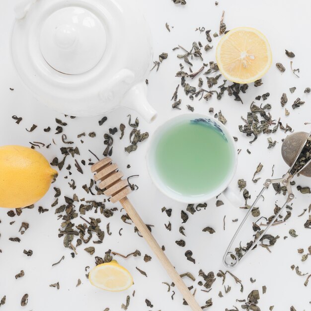 Dry tea leaves; tea strainer; lemon; fresh green tea; and teapot on white backdrop