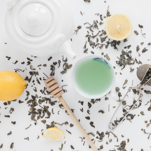 Dry tea leaves; tea strainer; lemon; fresh green tea; and teapot on white backdrop