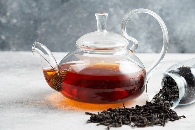 Dry tea leaves with teapot on marble.