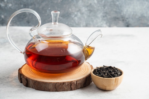 Dry tea leaves with teapot on wooden board.