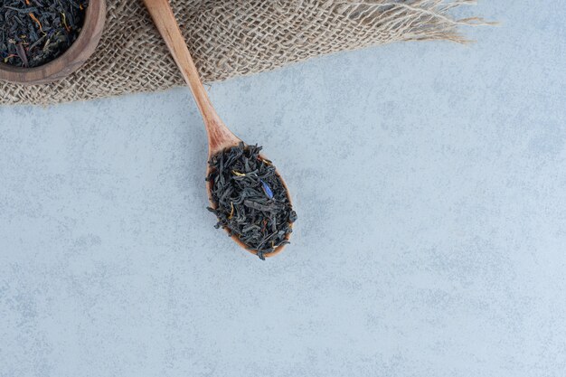 Dry tea leaves in the wooden bowl and spoon on towel on marble.