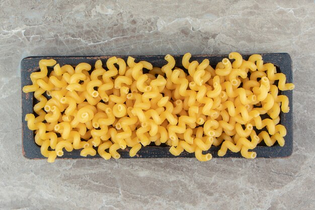 Dry uncooked pasta on black plate.