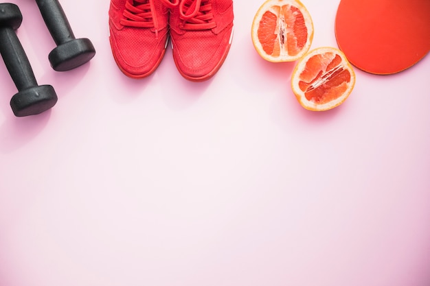 ダンベル;靴;ピンクの背景にオレンジ色の果物とピンポンラケット