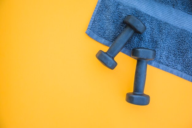 Dumbbells on towel over yellow background