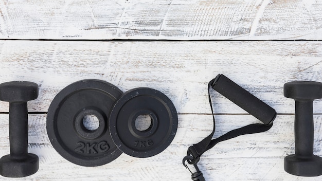 Dumbbells; weight plates and fitness strap on white wooden textured background