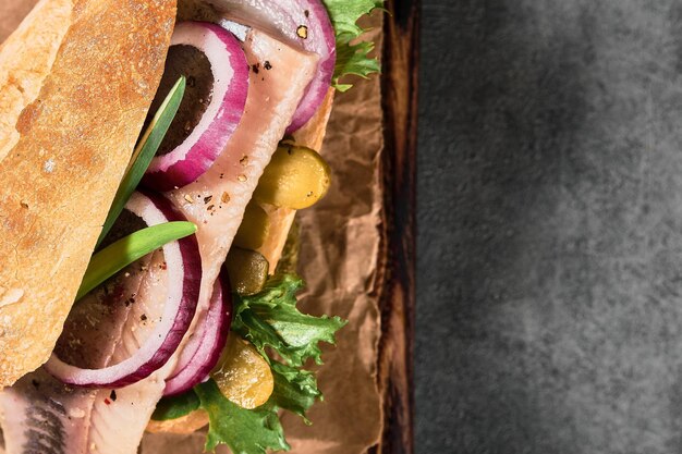 Dutch sandwich with herring, pickled cucumbers and red onions on a paper lining. Ingredients on a cutting board. Layout on the table, copy space