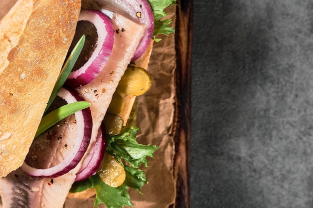 Dutch sandwich with herring, pickled cucumbers and red onions on a paper lining. Ingredients on a cutting board. Layout on the table, copy space